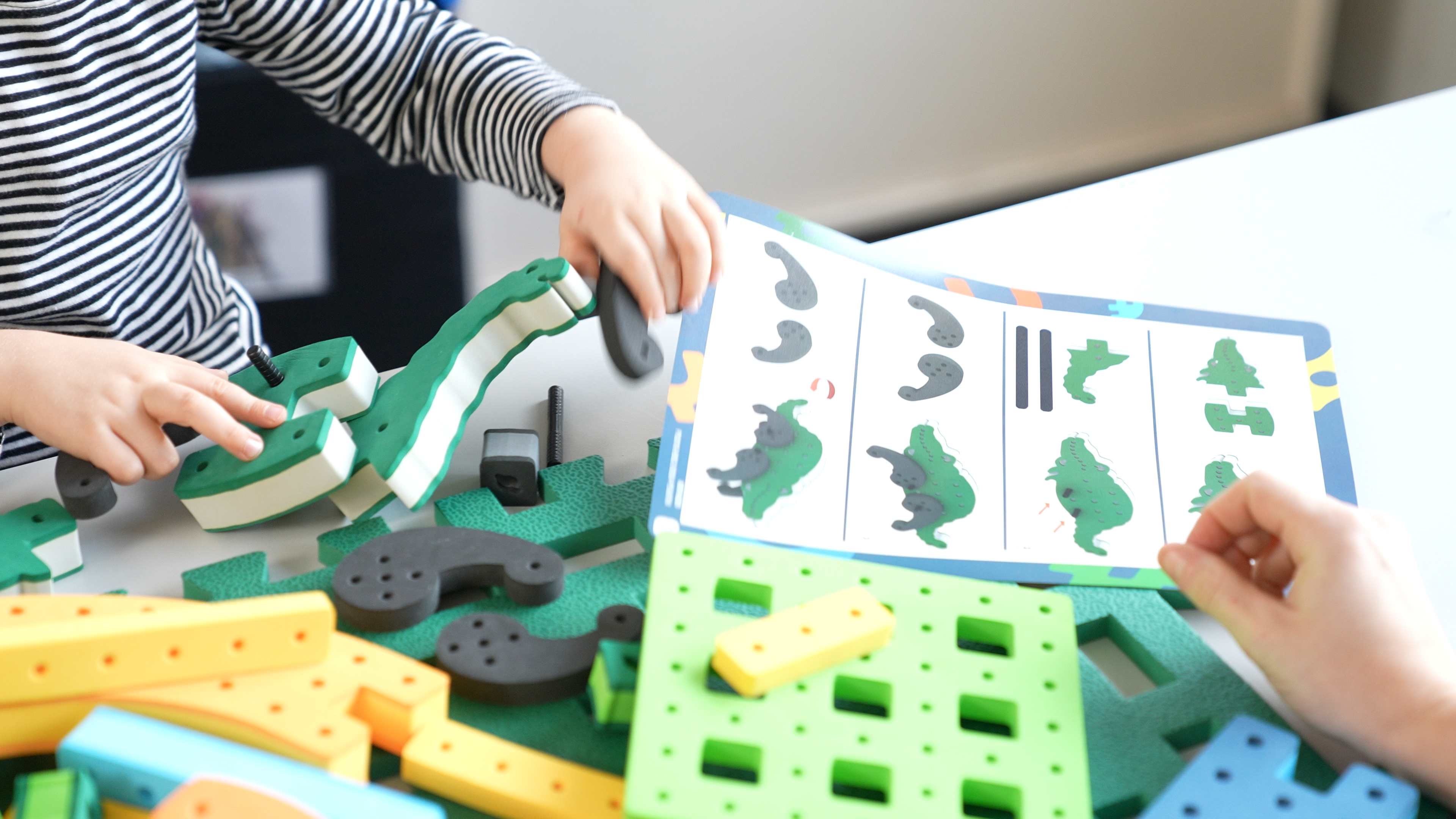 A child using a printed BAKOBA guide to build a structured model in a classroom setting.
