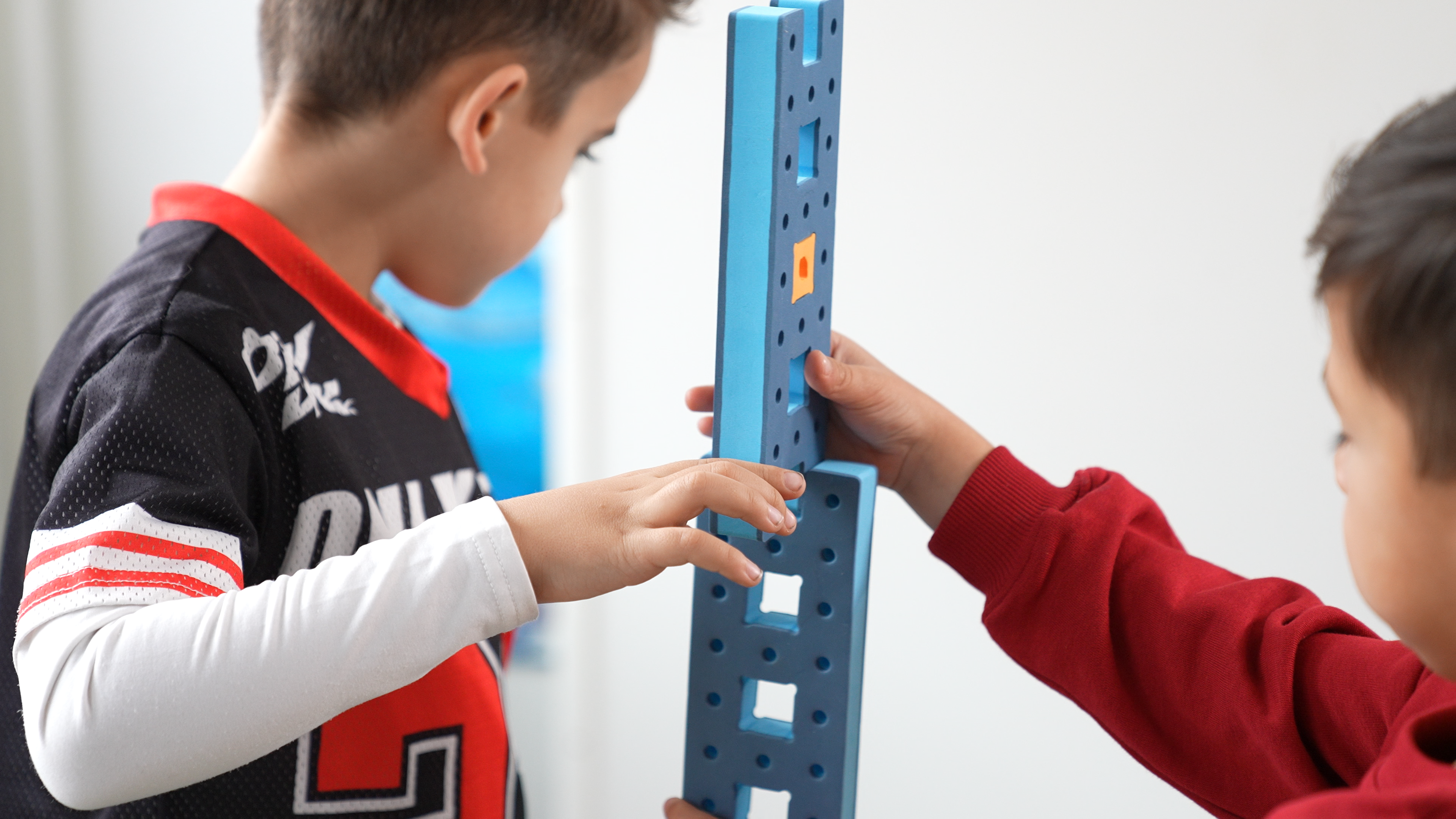 Two children collaborating on a large BAKOBA construction, demonstrating teamwork, creativity, and physical engagement.