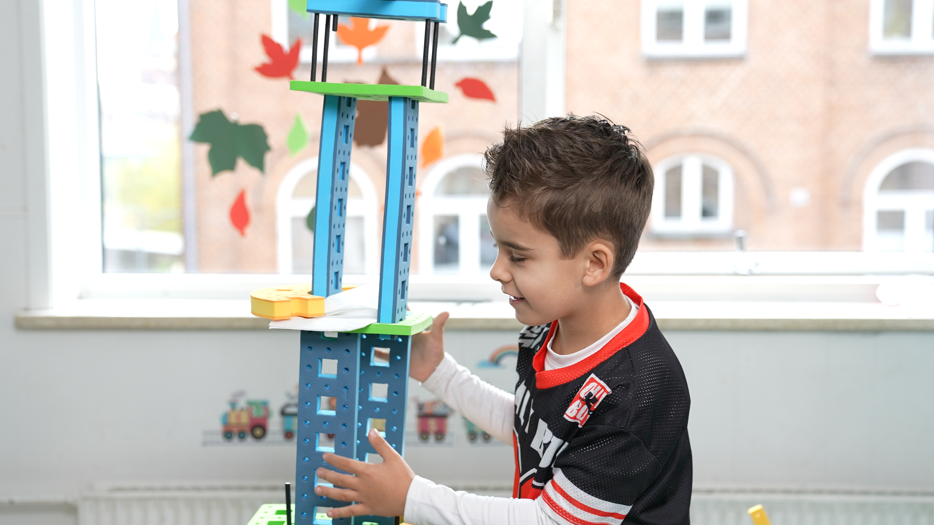 A child testing the stability of a tall BAKOBA construction, exploring balance and structural strength through play.